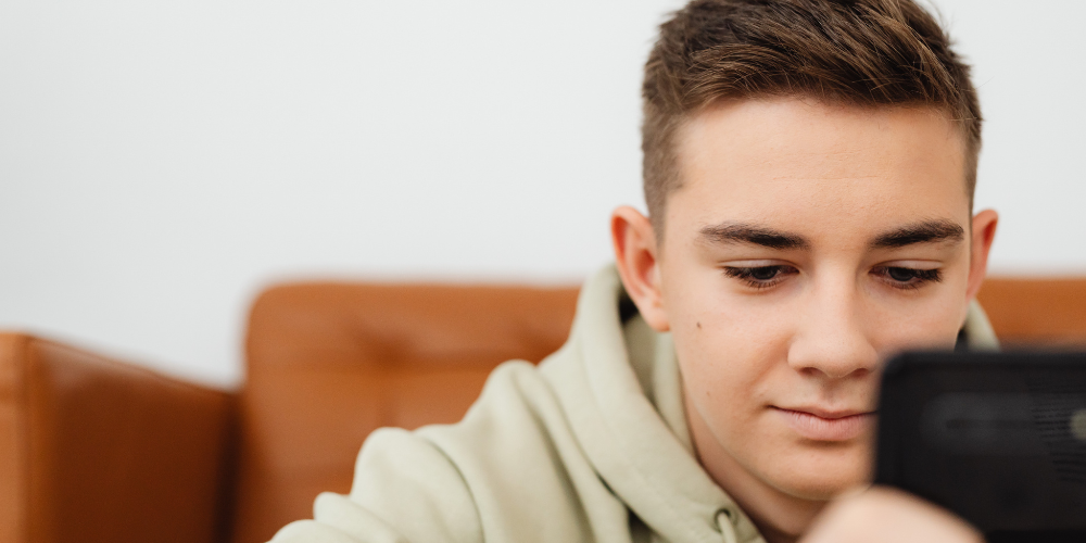 Image of teenage boy in a hoodie looking at his phone. 